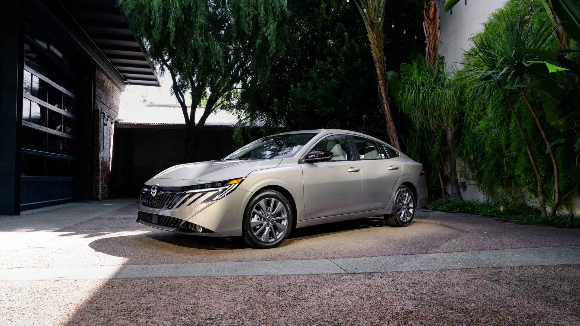 2025 Nissan Sentra® in silver parked outside a modern home with lush greenery and sleek front style.