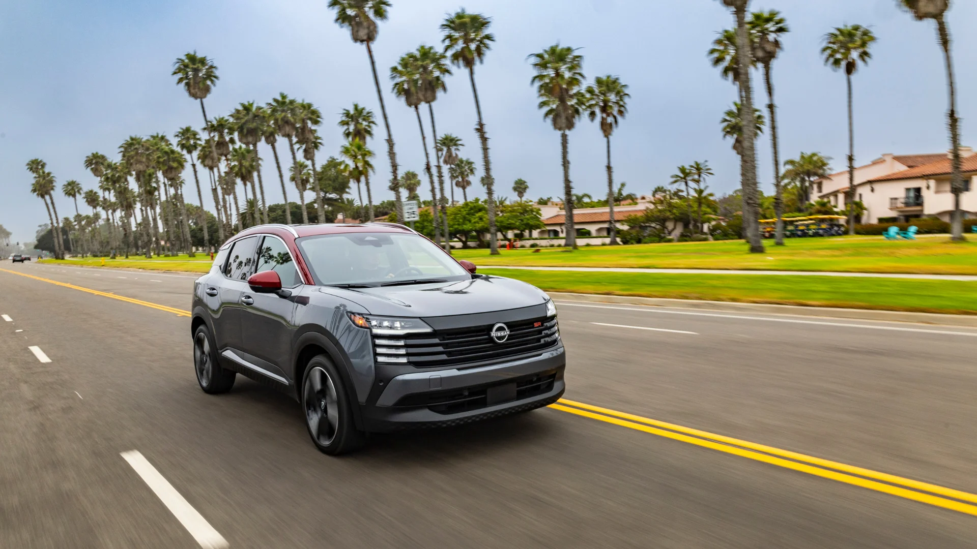 2026 Nissan Kicks® SR in gray with red roof driving on a palm-lined road in a sunny coastal setting.