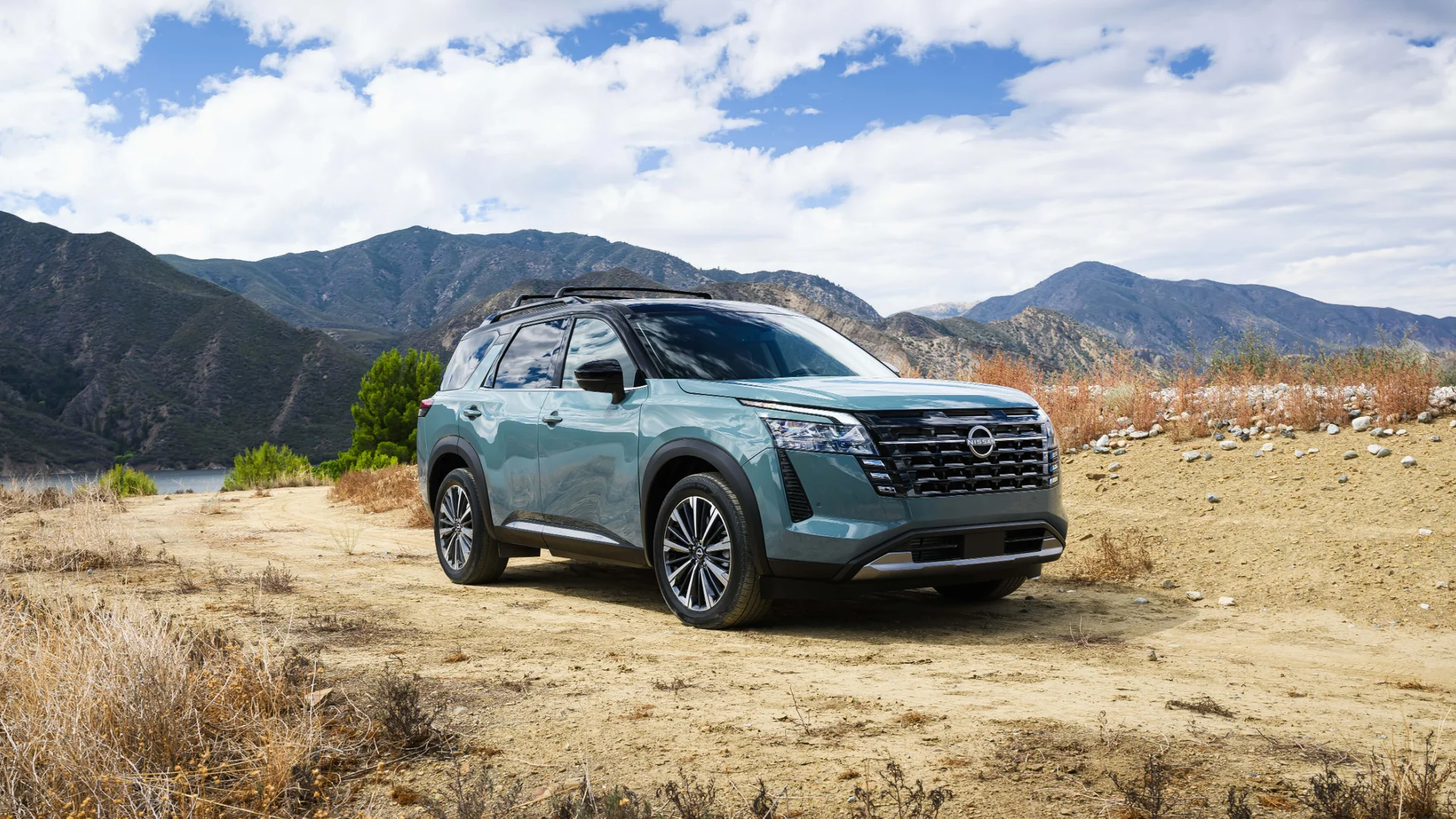 2026 Nissan Pathfinder® in light blue parked on rugged terrain with mountain and clear lake scenery.