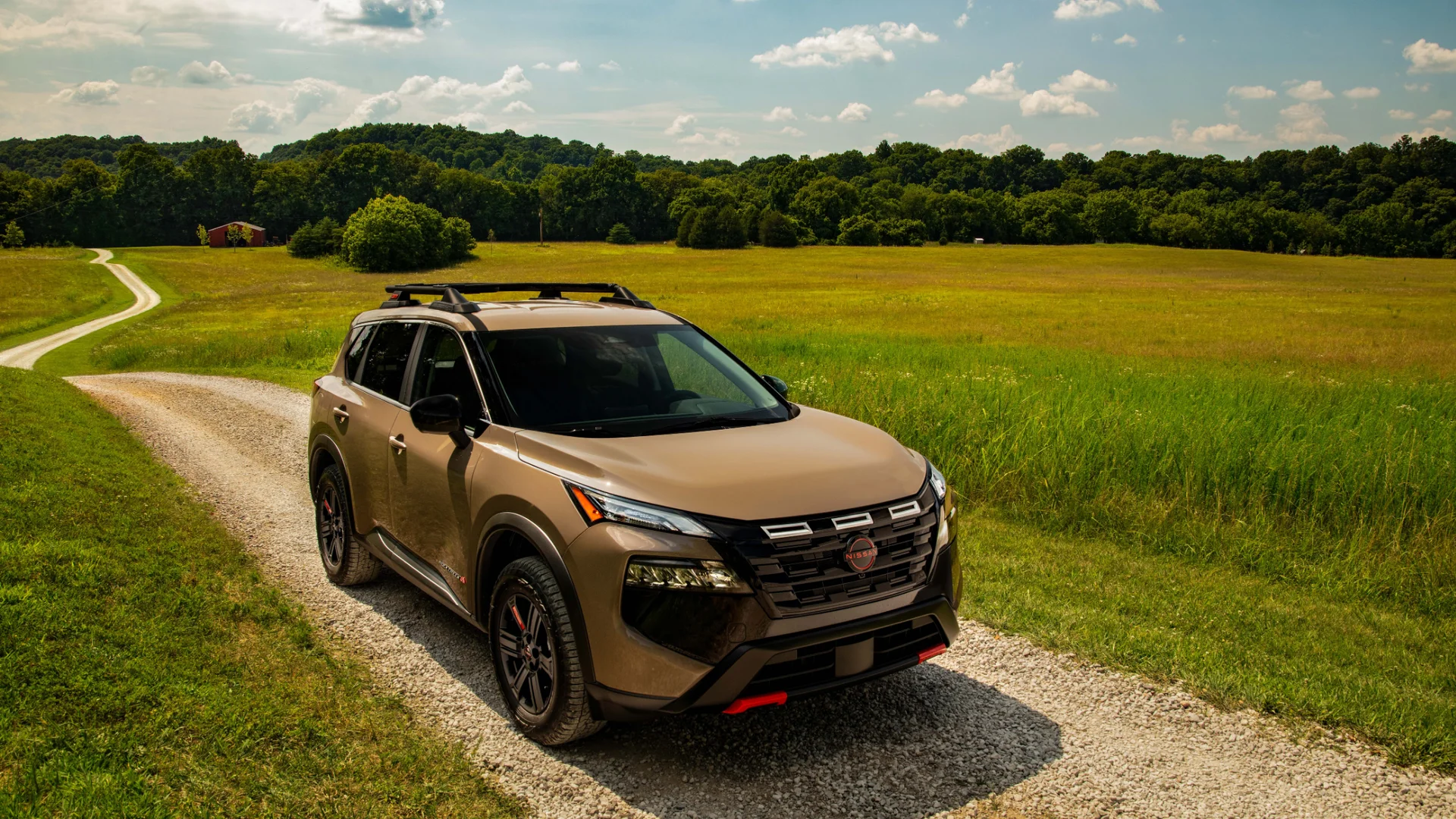 2026 Nissan Rogue® Rock Creek in bronze driving on a gravel route through rolling green countryside.