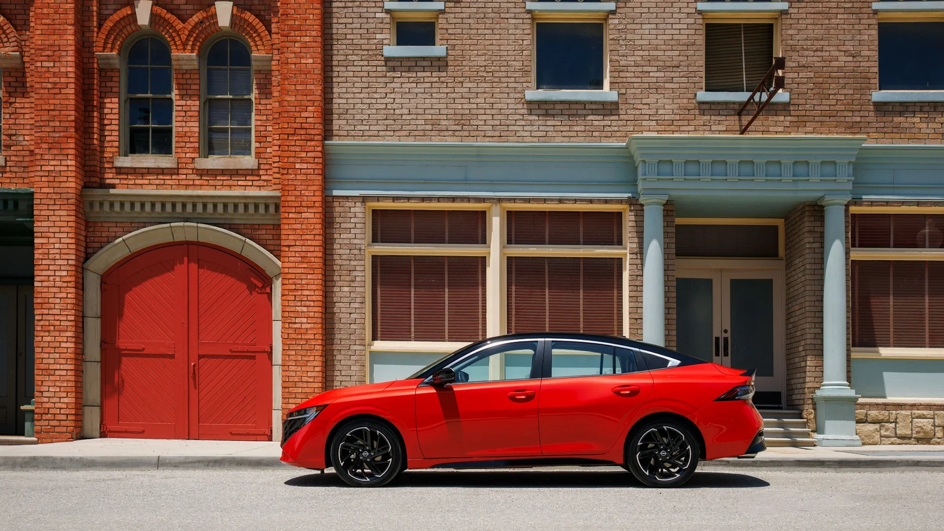 2025 Nissan Sentra® in red shown in a full side profile parked beside classic brick urban buildings.