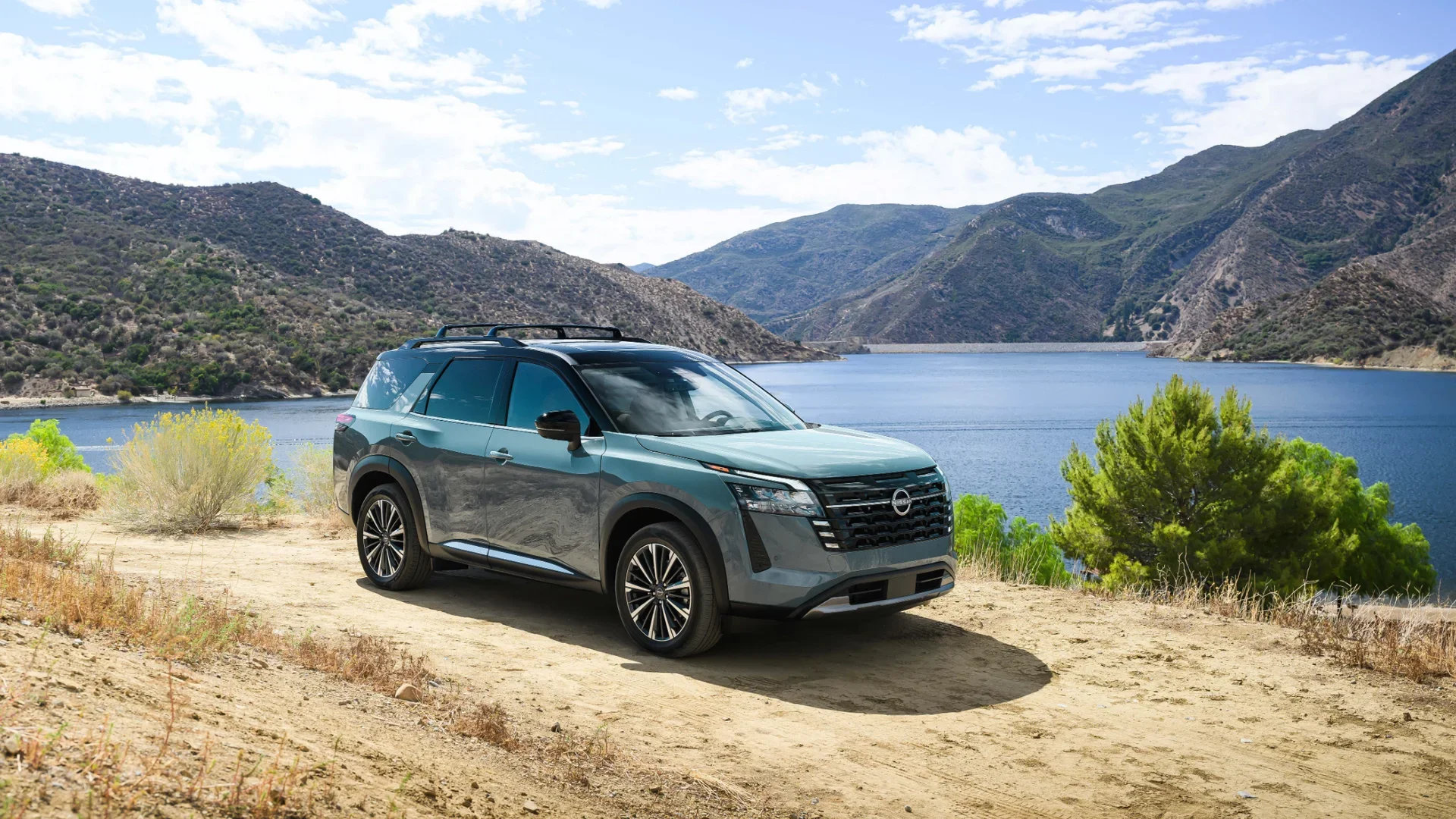 2026 Nissan Pathfinder® in blue parked beside a mountain lake with rocky hills and clear blue skies.